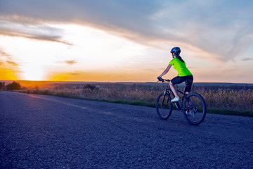 Fototapeta na wymiar Beautiful sport girl cyclist riding a bike on the road towards the sunset. Nature and recreation. Hobbies and sports