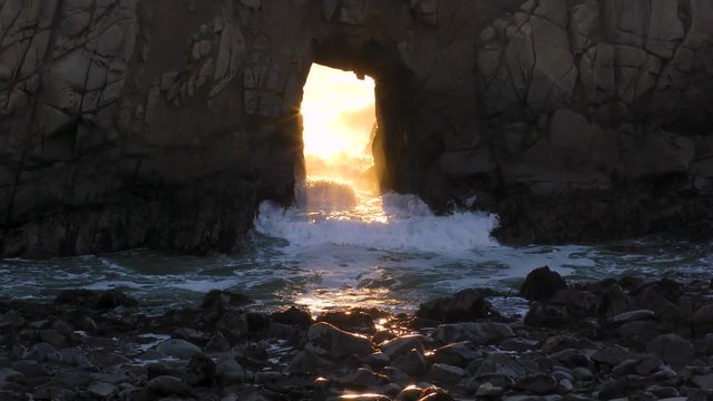 Amazing arched keyhole opening at sunset at Pfeiffer Beach California. The waves splash as the sun aligns with the canal at sunset at this location only one week a year. 