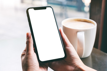 Mockup image of hands holding black mobile phone with blank screen with coffee cup on wooden table