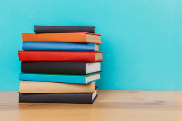 A simple composition of many hardback books, raw books on a wooden table and a bright blue background