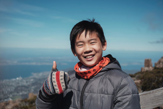 Happy and confident tween mixed race Asian boy smiling and giving thumb up over mountain view, preteen travel in winter concept