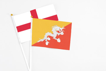 Bhutan and England stick flags on white background. High quality fabric, miniature national flag. Peaceful global concept.White floor for copy space.