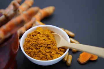 Composition with bowl of turmeric powder on black background.