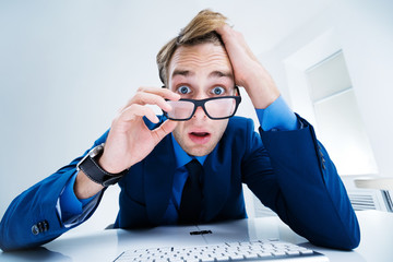 Shocked or surprised confident businessman in blue suit and glasses, working with computer at...