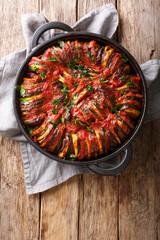 Baked zucchini, potatoes, eggplant and onions in tomato sauce close-up in a pan. Vertical top view