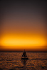 Obraz na płótnie Canvas Sunset at Santa Monica pier: sailing boat on the horizon