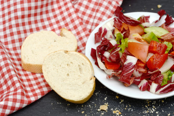 mixed salad and rustic crusty white bread lying on black slate on red white towel in the kitchen