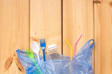 Disposable plastic utensils are scattered on wooden background. Ecology problem. Environmental pollution. Flat lay. Top view. Copy space.