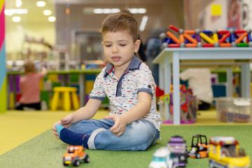 Young caucasian kid playing at kindergarten with toy cars. Preschooler boy happy at playroom