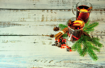 Two glasses of mulled wine with slices of fruit and spices, stand on a wooden table surrounded by...