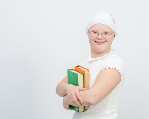 A girl with Down Syndrome stands with books on gray background. Empty space for text