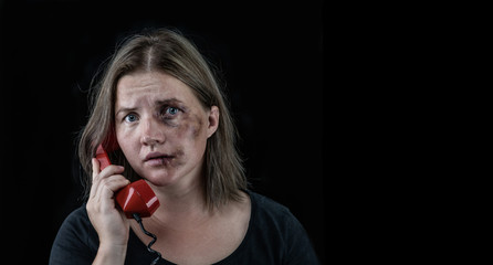 Woman victim of domestic violence and abuse asks for help by phone. Empty space for text. Isolated on dark background