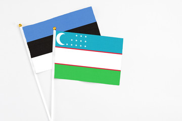 Uzbekistan and Estonia stick flags on white background. High quality fabric, miniature national flag. Peaceful global concept.White floor for copy space.