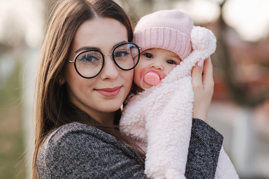 Portrait of mother and her little baby girl. Beautiful mom and cute baby. Mother hud her daughter. Baby dressed in peanch colour hat and nipple toy. Mom kiss her daughter