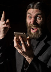 strange bearded senior priest with a smartphone, bearded old man is calling on a dark background