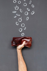 Concept of earning money with a brown leather wallet held in a hand in front of a blackboard with hand drawn coins