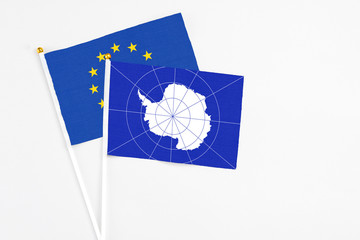 Antarctica and European Union stick flags on white background. High quality fabric, miniature national flag. Peaceful global concept.White floor for copy space.