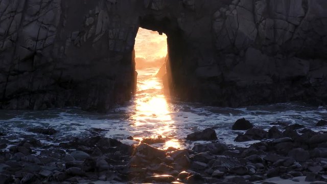 Sunlight streams through a keyhole arched rock at Pfeiffer beach at Big Sur located on the Pacific Ocean on the coast of California at sunset. 