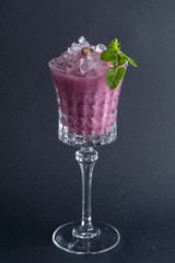 Purple alcoholic cocktail with blueberry and mint leaf isolated on dark background