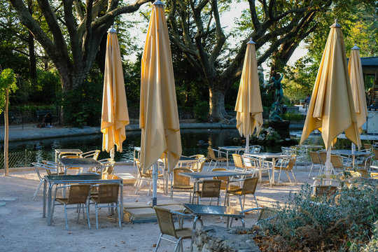 Terrace with  empty metal tables and closed yellow umbrellas by the water in the park. Provence tourism. Avignon.