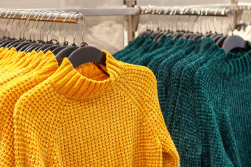 Colored sweaters hanging on hangers in store women's clothing