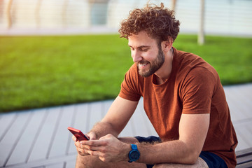 Young adult man using modern cellphone in the park.