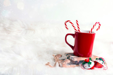 Obraz na płótnie Canvas Red mug with candy canes on toy sled over white fur background.