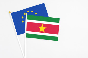 Suriname and European Union stick flags on white background. High quality fabric, miniature national flag. Peaceful global concept.White floor for copy space.