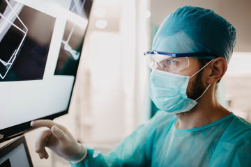 surgeon in uniform and glasses examines an X-ray image of a bone fracture in the operating room.