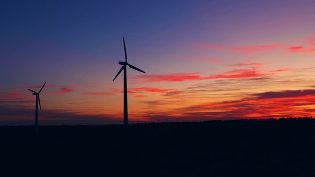 Sunset burning sky and windmills silhouette on the industrial technology field