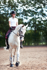 Young pretty teenage girl equestrian practicing horseback riding on manege
