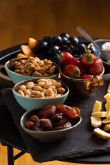 Cheese and fruits plate with glass of white wine on round tray, colorful and delicious charcuterie with snacks and wineglass for romantic evening, wine tasting, selective focus.