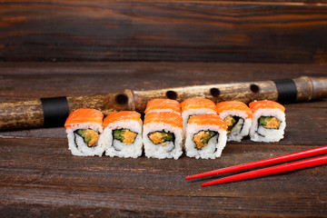 Fresh sushi roles on a wooden plate with hands of the chef in the background