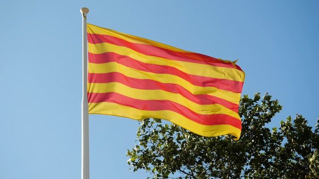 Close-up shot of the flag of Catalonia flying in the wind against blue sky. Barcelona. Spain. Slow motion. HD