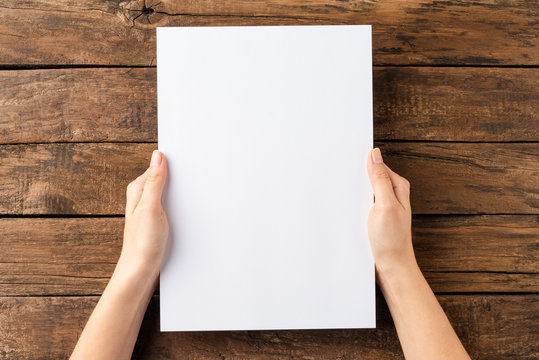 Overhead shot of woman’s hands holding blank paper sheet on rustic wooden table. Close up
