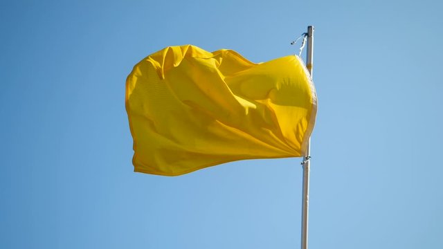 Yellow flag flying in the wind on the beach against blue sky. Slow motion. HD