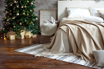 Christmas apartment decor, Scandinavian cozy home decor, bed with warm knitted blankets next to the Christmas tree. Lights and garlands