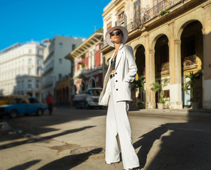 Stylish woman in a white suit and white hat on a city street. Cuba