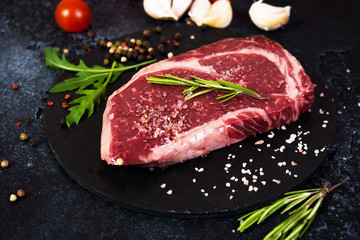 Close up Raw fresh marbled beef steak centered on a charcoal stand with salt and herbs. Horizontal orientation.