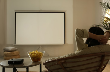 Young woman watching movie using video projector at home