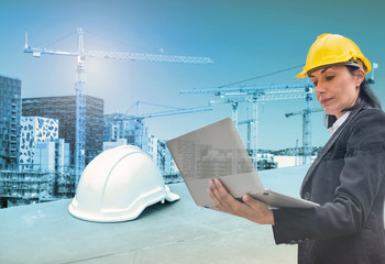 Woman engineer holding laptop with helmet on construction building with cranes