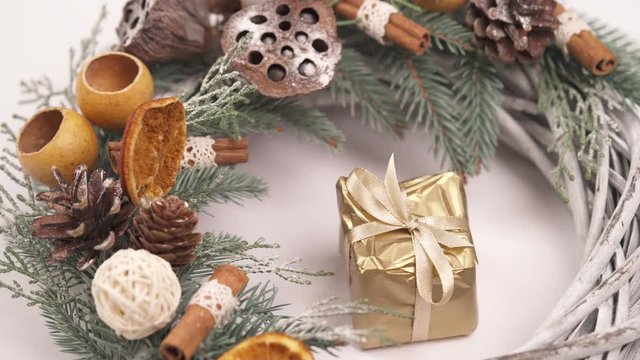 Top view of a female hand putting tiny gift box wrapped with golden paper and decorated with silky yellow ribbon to the advent wreath. Christmas traditions concept.