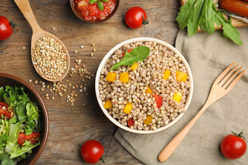 Tasty buckwheat porridge with vegetables on wooden table, flat lay