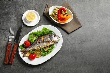 Delicious roasted fish with lemon on dark grey table, flat lay