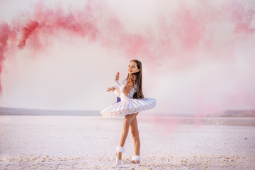 Tender young ballerina dancer in a snow-white tutu dress and white pointe shoes in pink smoke.  on...