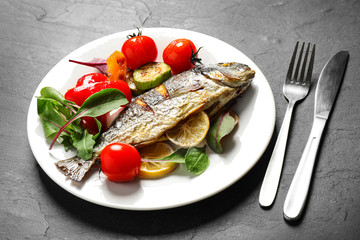 Delicious roasted fish with lemon and vegetables on dark grey table