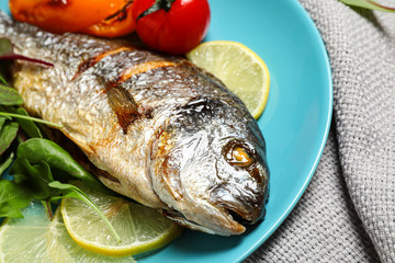 Delicious roasted fish with lemon and vegetables on plate, closeup
