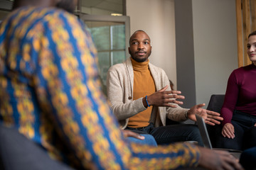 Creative black businessman talking in interview casually with fellow diverse South African coworkers