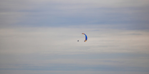 Paraglider floating through clouds and blue sky over Camps Bay, Cape Town.