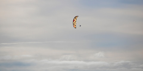 Paraglider floating through clouds and blue sky over Camps Bay, Cape Town.